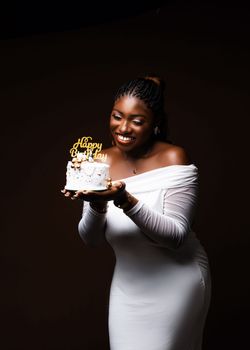 A joyful woman in a white dress holding a birthday cake with candles.