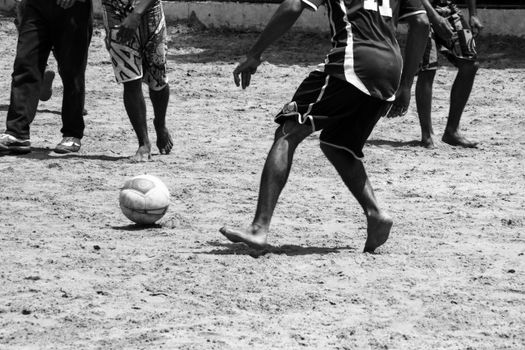 Dynamic scene of barefoot men playing soccer on a sandy beach.