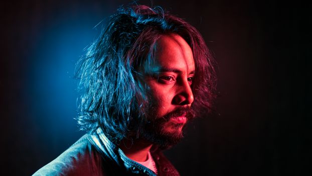 Close-up portrait of a bearded man with colored lighting, conveying a dramatic and artistic mood.
