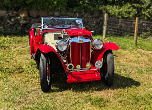 Classic red MG sports car parked on grass, highlighting its vintage charm and sleek design.