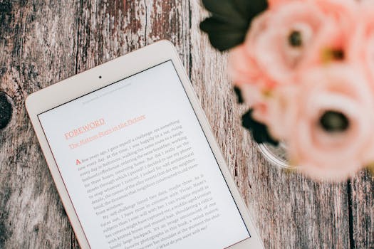 Close-up of a tablet displaying text on a wooden table with flowers.