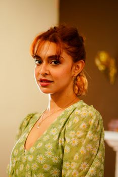 Warm portrait of a woman with red hair wearing a green floral dress indoors.