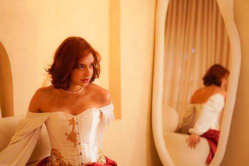 Free Woman wearing a corset poses beside a mirror with a warm vintage vibe. Stock Photo