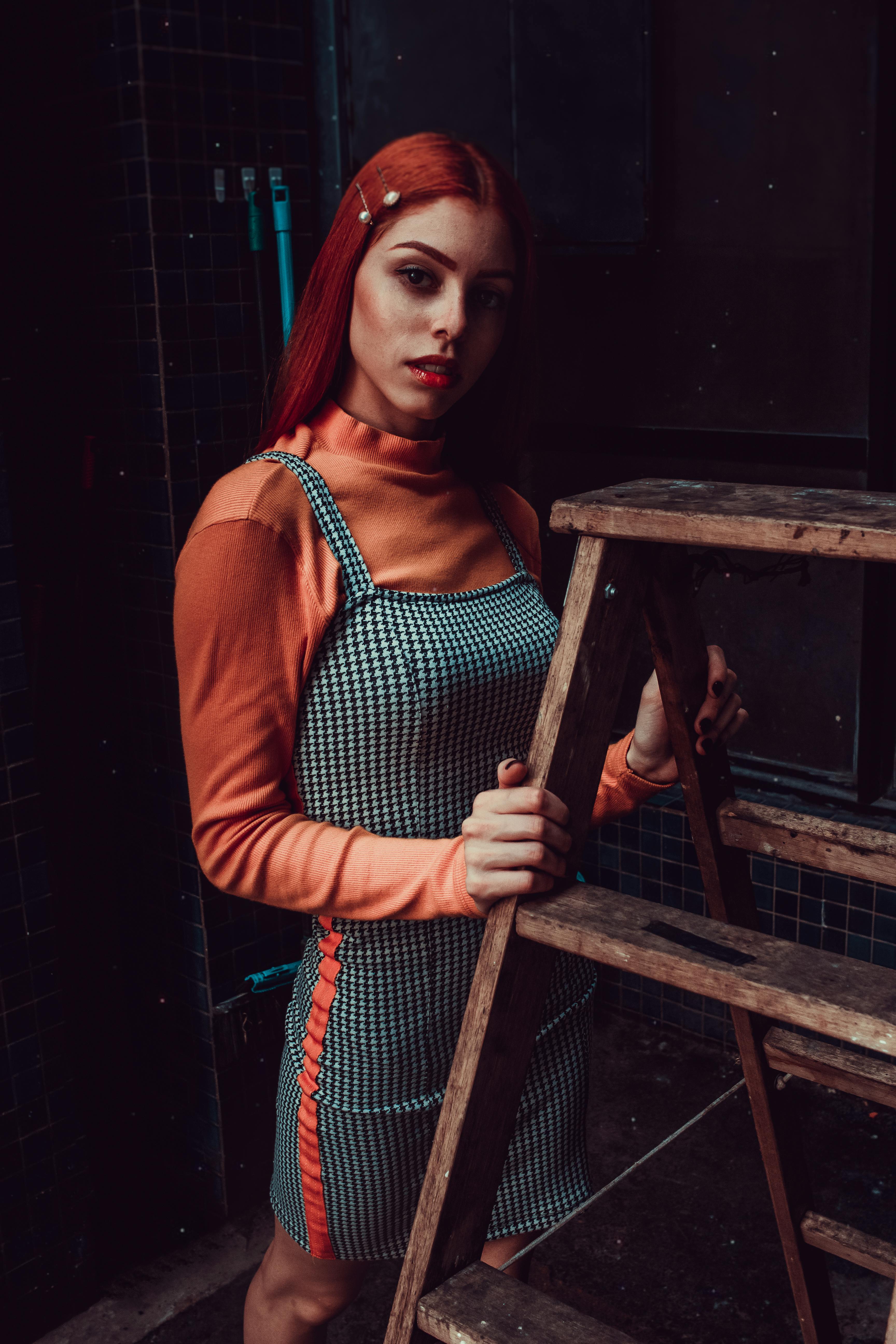 一位红发时尚女子站在室内质朴的木梯旁