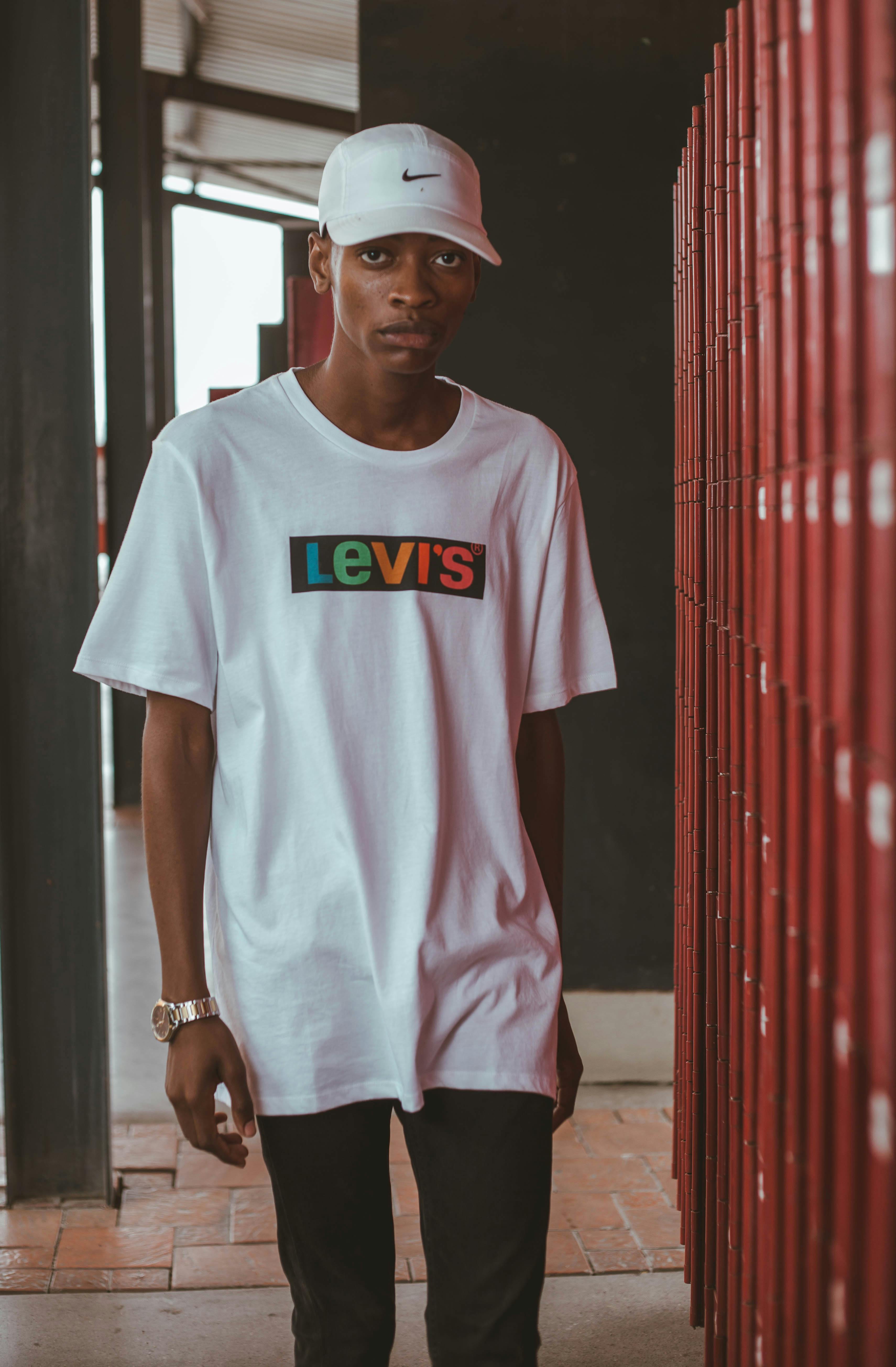Stylish young man in white shirt and cap standing near lockers indoors.