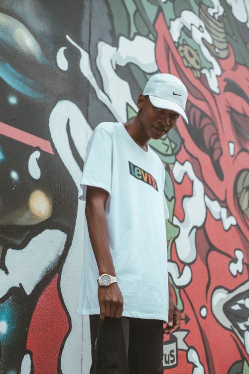 Free A stylish young man in casual wear poses against a graffiti wall, showcasing urban culture. Stock Photo