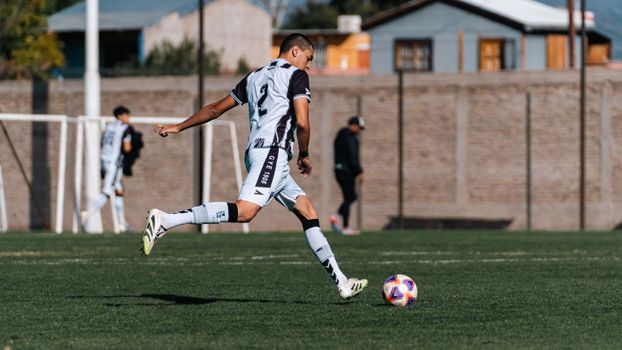 Dynamic shot of a young soccer player kicking a ball during a match on a sunny day.
