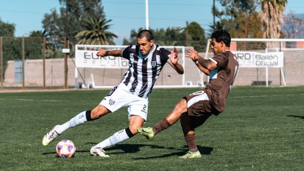 Two soccer players compete fiercely on a sunny day outdoor field.