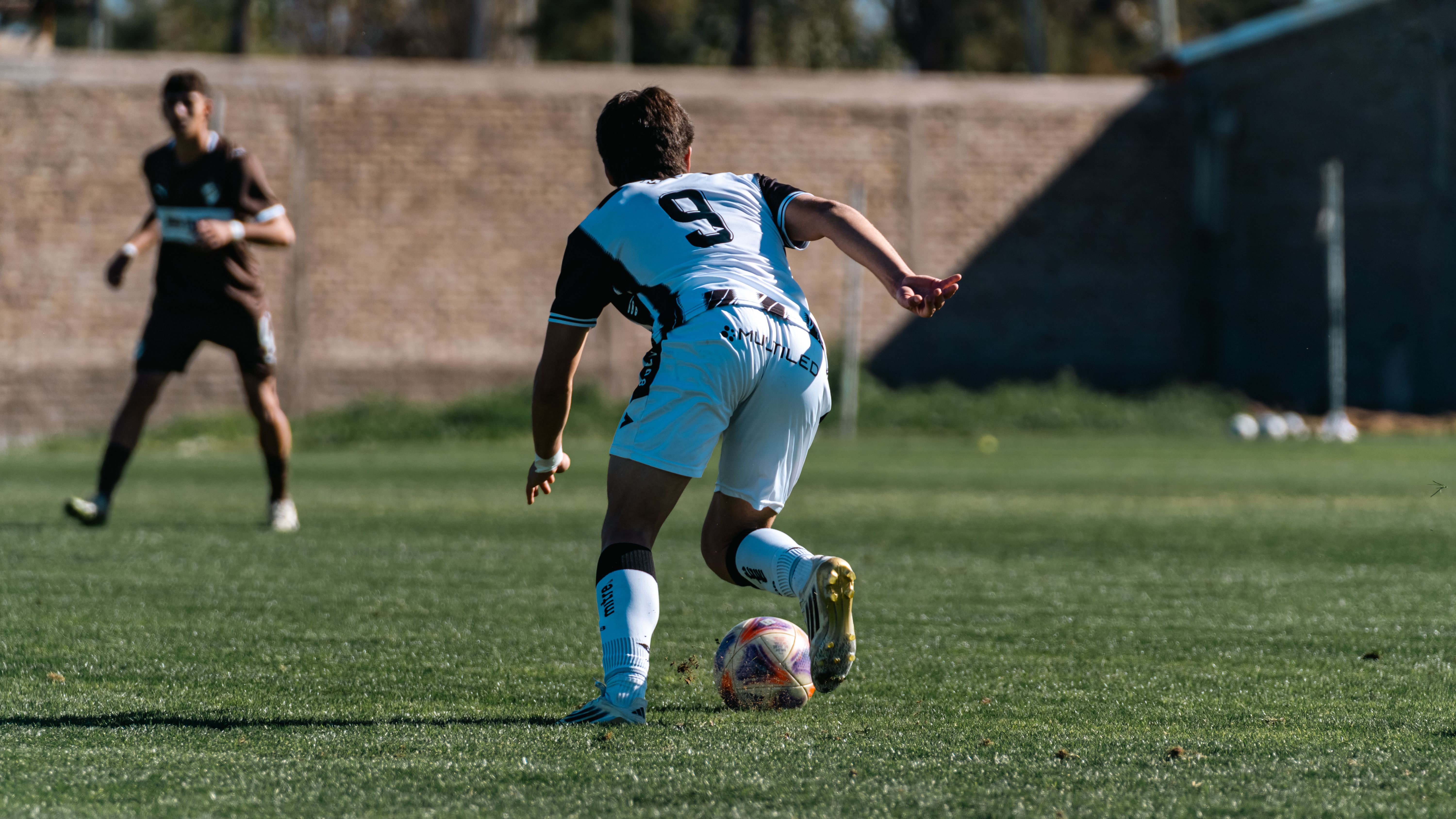 Soccer player dribbles during a match on a sunlit outdoor field with dynamic motion.
