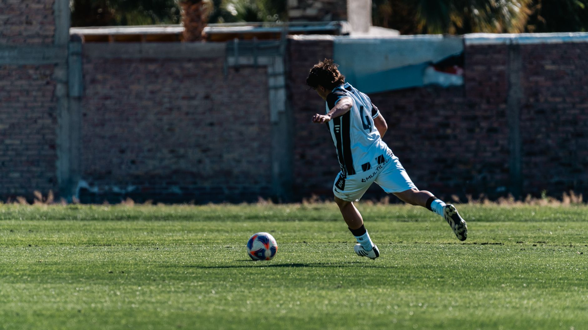 midfielder completing shuttle runs between yellow cones while teammates recover beside a full-size goal