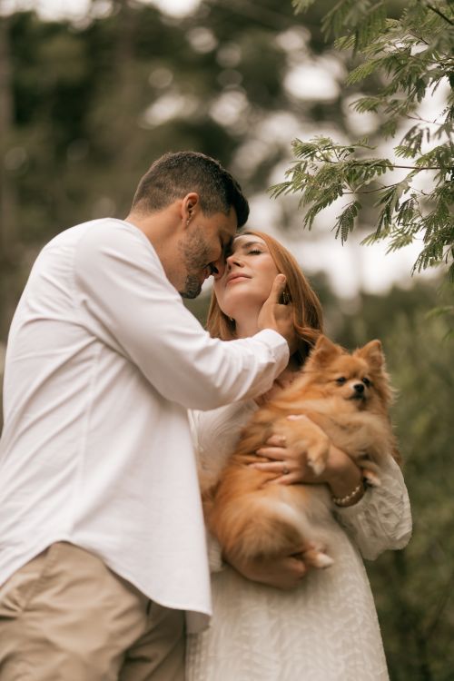 Free Couple embraces lovingly with their Pomeranian dog in a serene outdoor setting. Stock Photo