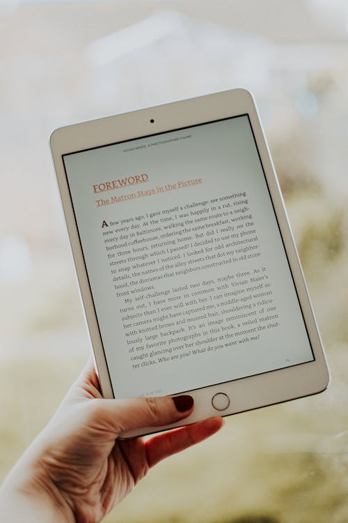 Free Close-up of a hand holding a tablet displaying an e-book page. Stock Photo