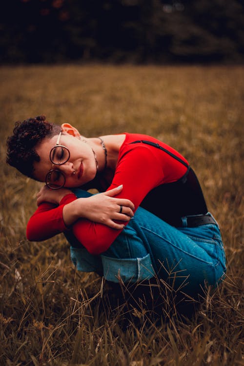 Woman in Red Top and Blue Denim Jeans Sitting on Grass Field