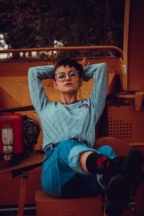 Free A woman in denim jeans and gray sweater posing against industrial machinery. Stock Photo