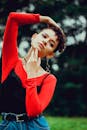 一位年轻女子身着充满活力的红色上衣，在户外模糊的绿色背景前沉思地摆着姿势