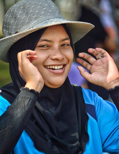 Cheerful woman in hijab adjusting her hat outdoors, exuding joy and positivity