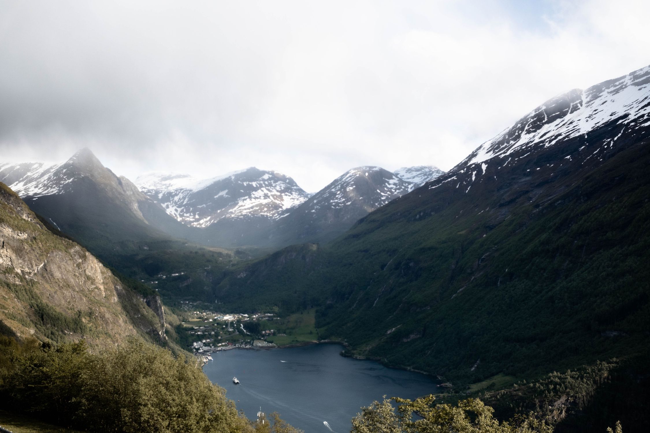 Breathtaking landscape of Geirangerfjord surrounded by snow-capped mountains and lush greenery in Norway.