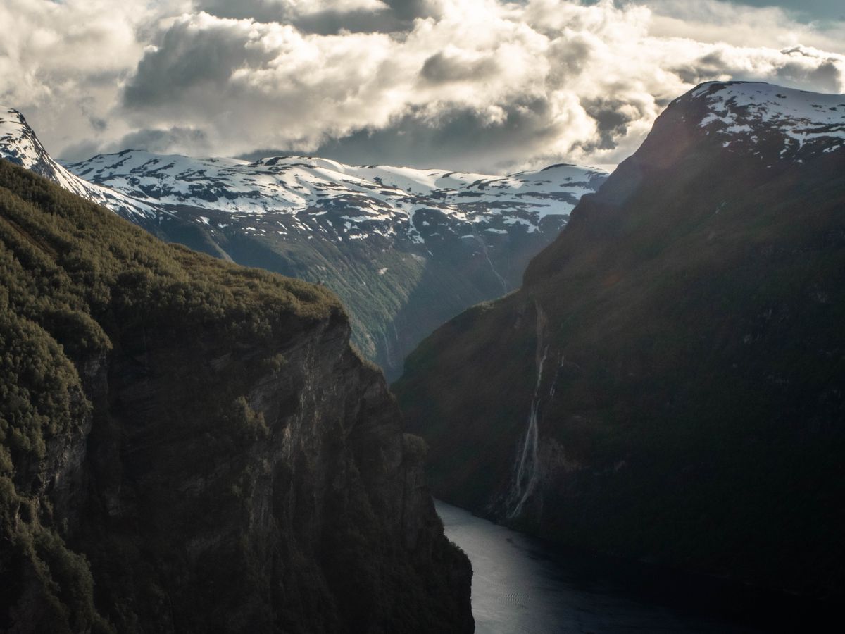 Sheer dark walls closing in on a narrow arm of a Norwegian fjord under heavy cloud.