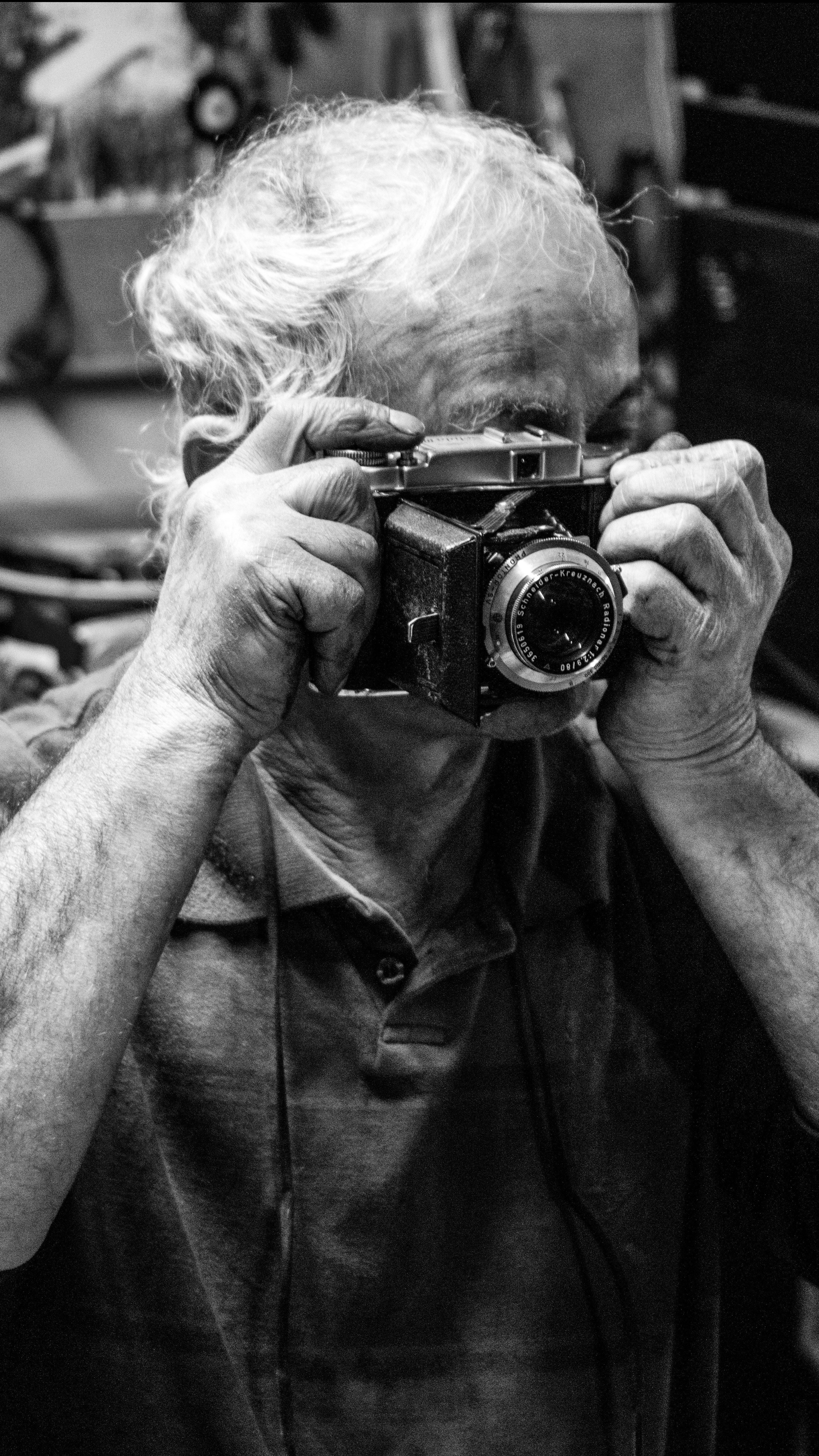 A senior adult captures a moment with a vintage camera in a black and white portrait.
