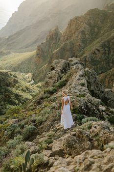 Woman in white dress hikes along a rocky mountain path in Greece.