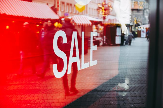 Red banner with sale inscription in fashion shop showcase with glass walls reflecting people walking on street