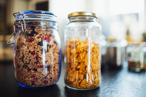 Glass jars with healthy cornflakes and muesli placed  on table in kitchen