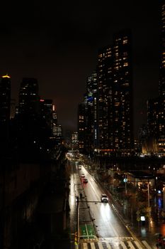 Nighttime cityscape of Sydney with illuminated skyscrapers reflecting on wet roads.