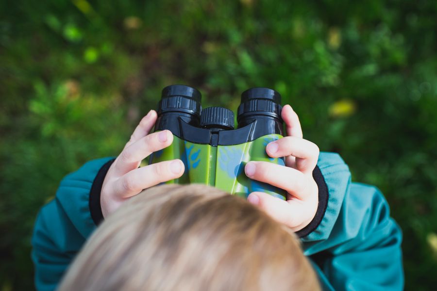 A child explores nature using binoculars in a grassy environment. Perfect for adventure themes. Stock Photo