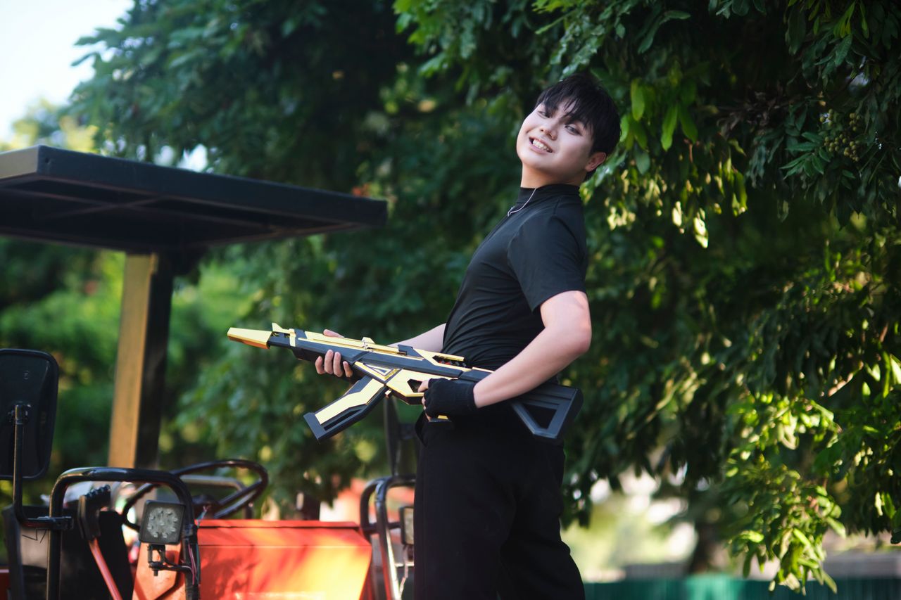a cheerful teenager with a toy rifle poses outdoors in vietnam under l