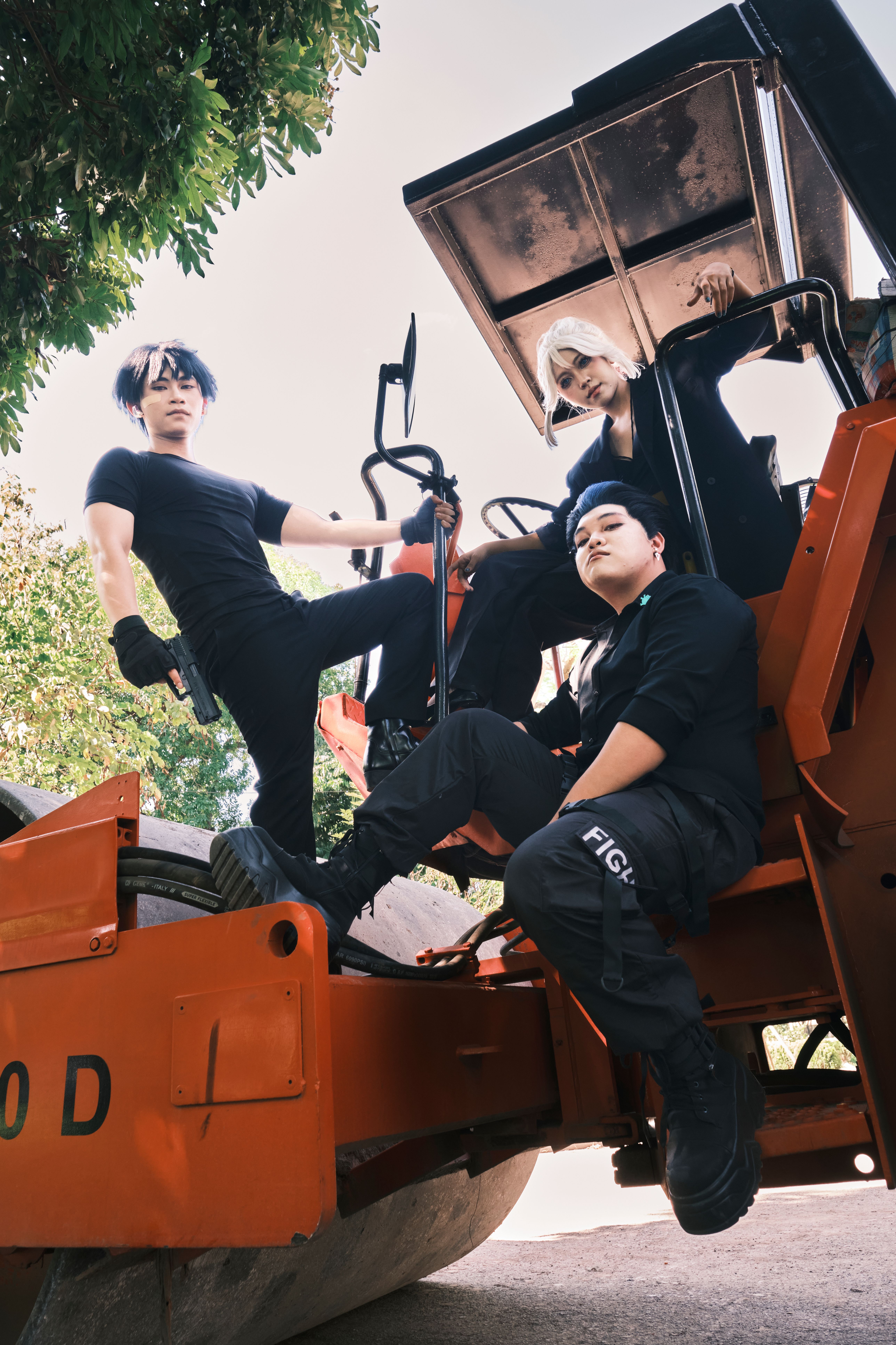 Three individuals pose confidently on an orange construction vehicle, highlighting modern fashion in an outdoor setting.