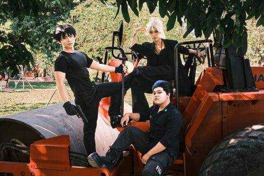 Three cosplayers pose on a road roller in a Vietnamese park, showcasing creative costumes.