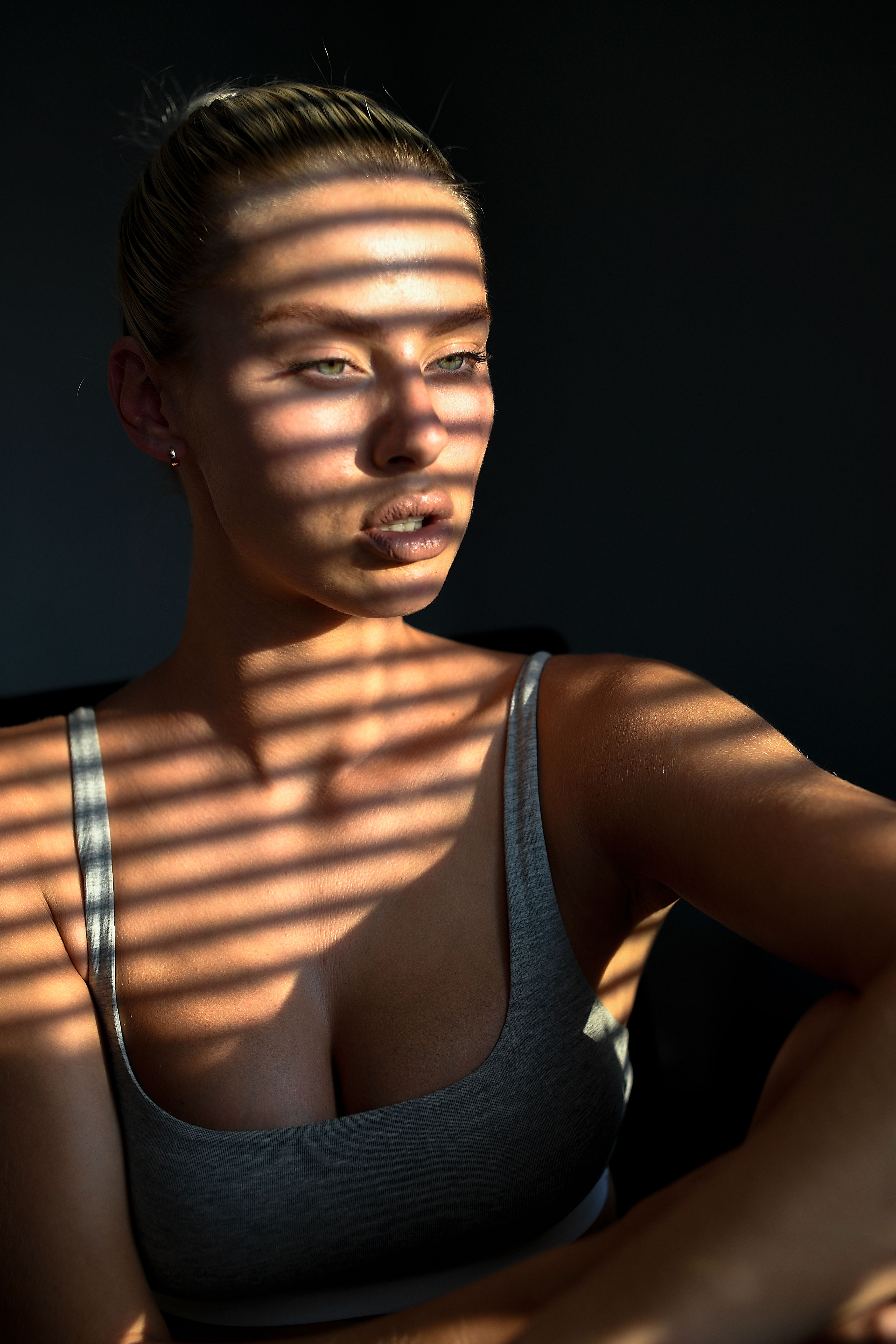 Captivating indoor portrait featuring dramatic light patterns from window blinds on a woman.