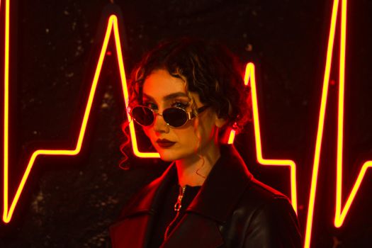 Portrait of a stylish woman in sunglasses and leather jacket against glowing neon heartbeat line.