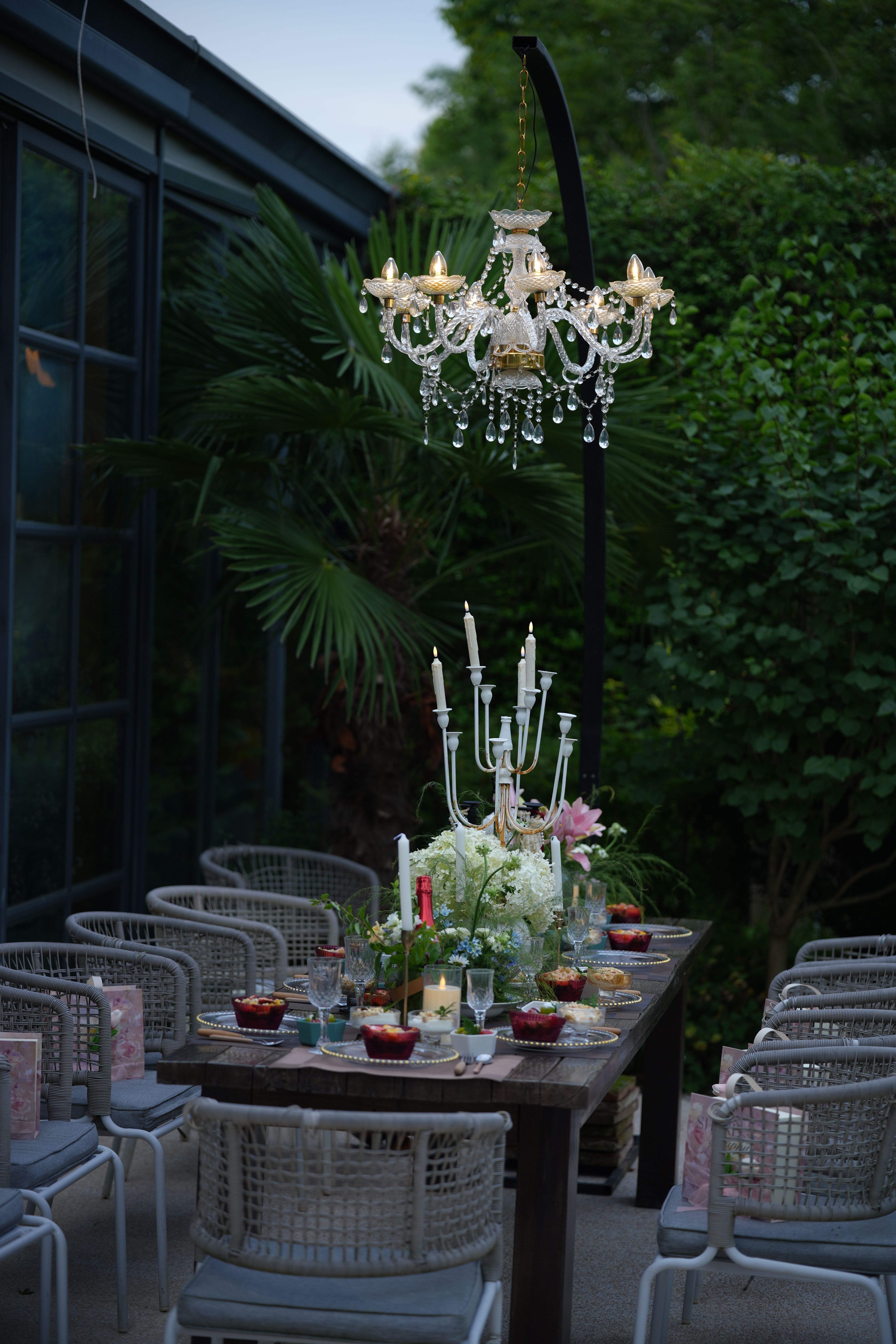 Luxurious outdoor dining table adorned with floral centerpiece and chandelier lighting.