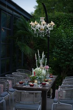 Luxurious outdoor dining table adorned with floral centerpiece and chandelier lighting.