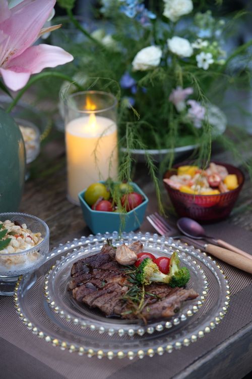 Free Chic outdoor dining setup featuring a grilled steak with vegetables, surrounded by floral decor and candlelight. Stock Photo