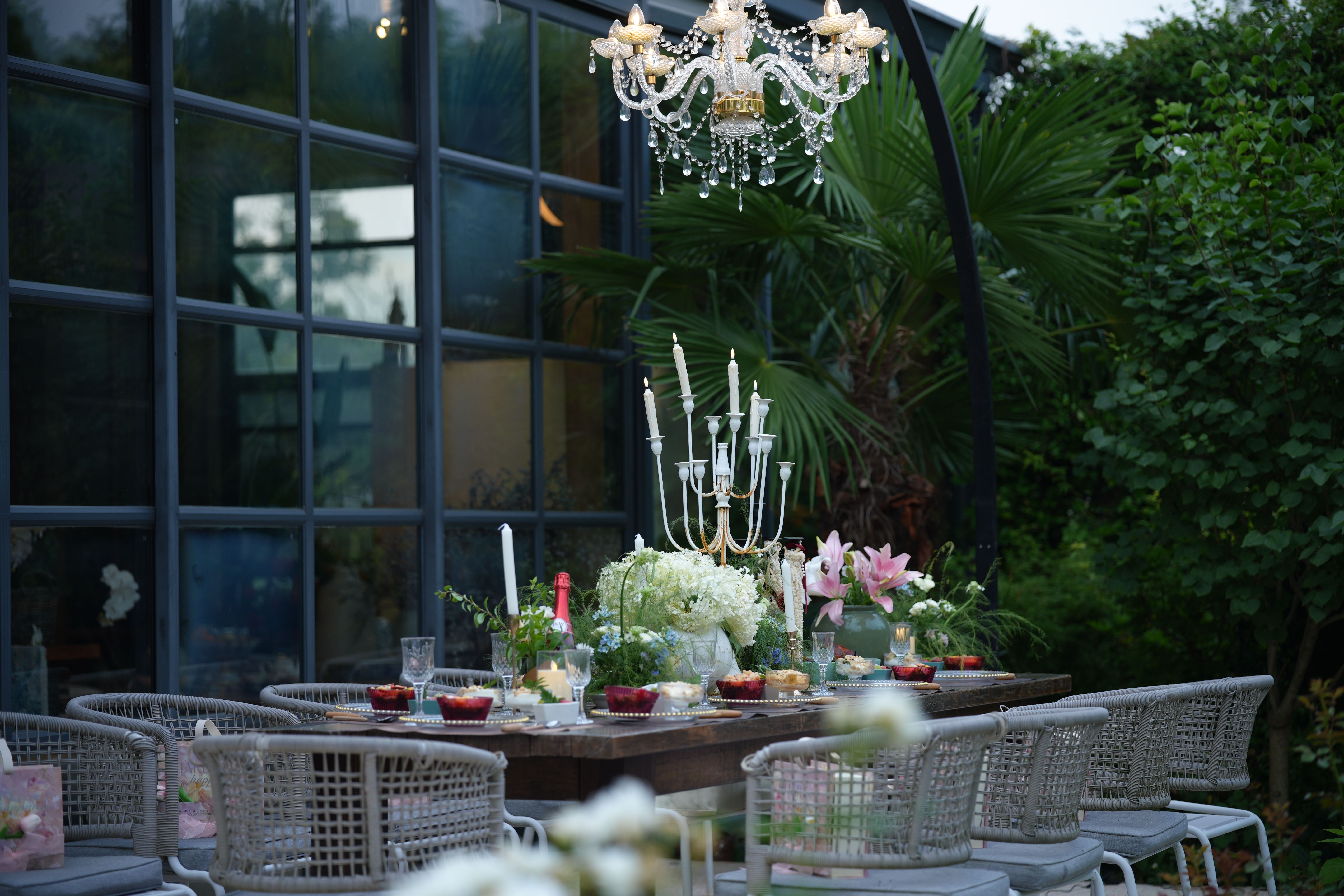 A beautifully set outdoor dining table with chandeliers and floral decorations, perfect for summer gatherings.
