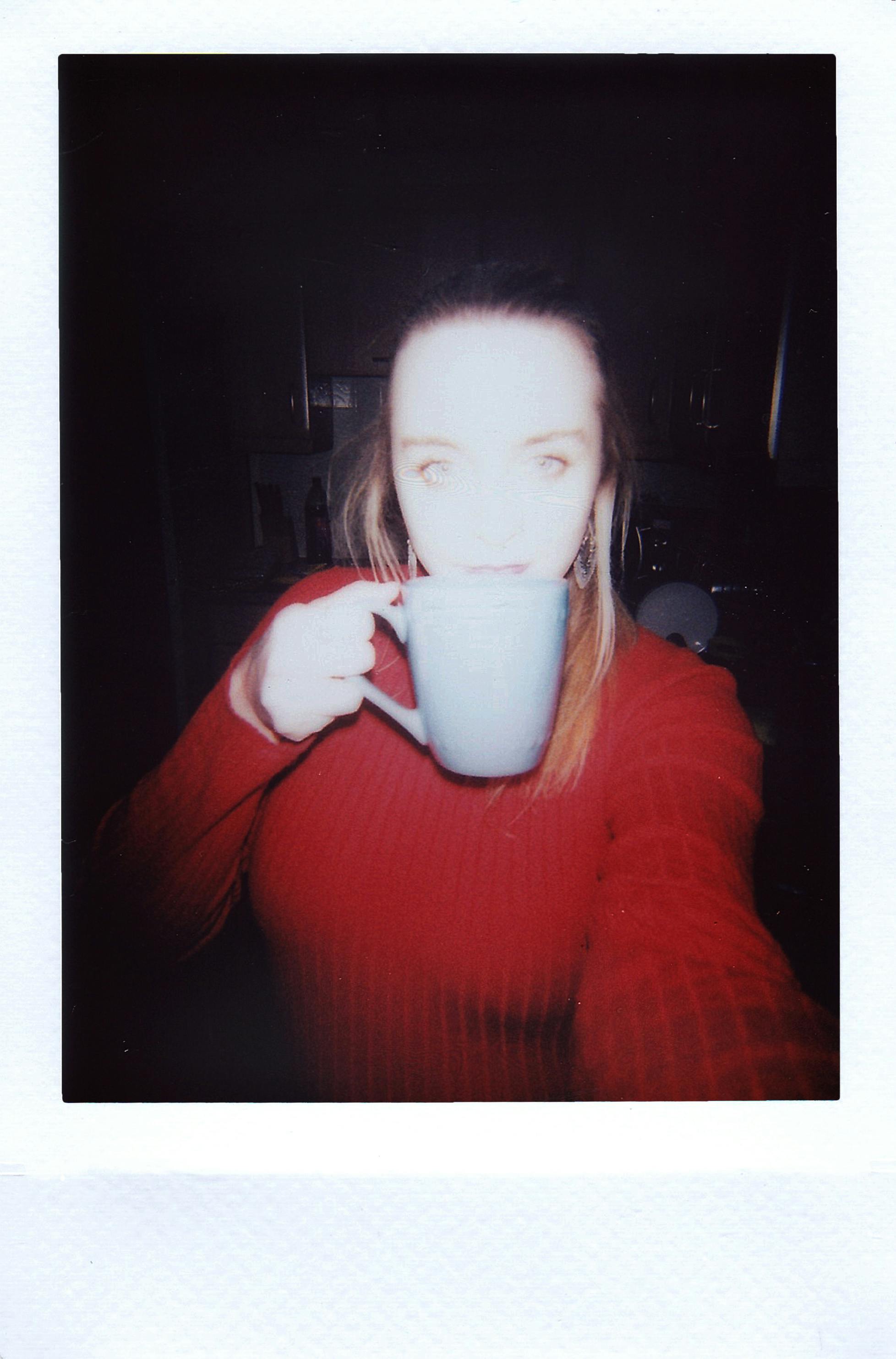 A woman in a red sweater drinks from a mug, captured in a cozy indoor setting.