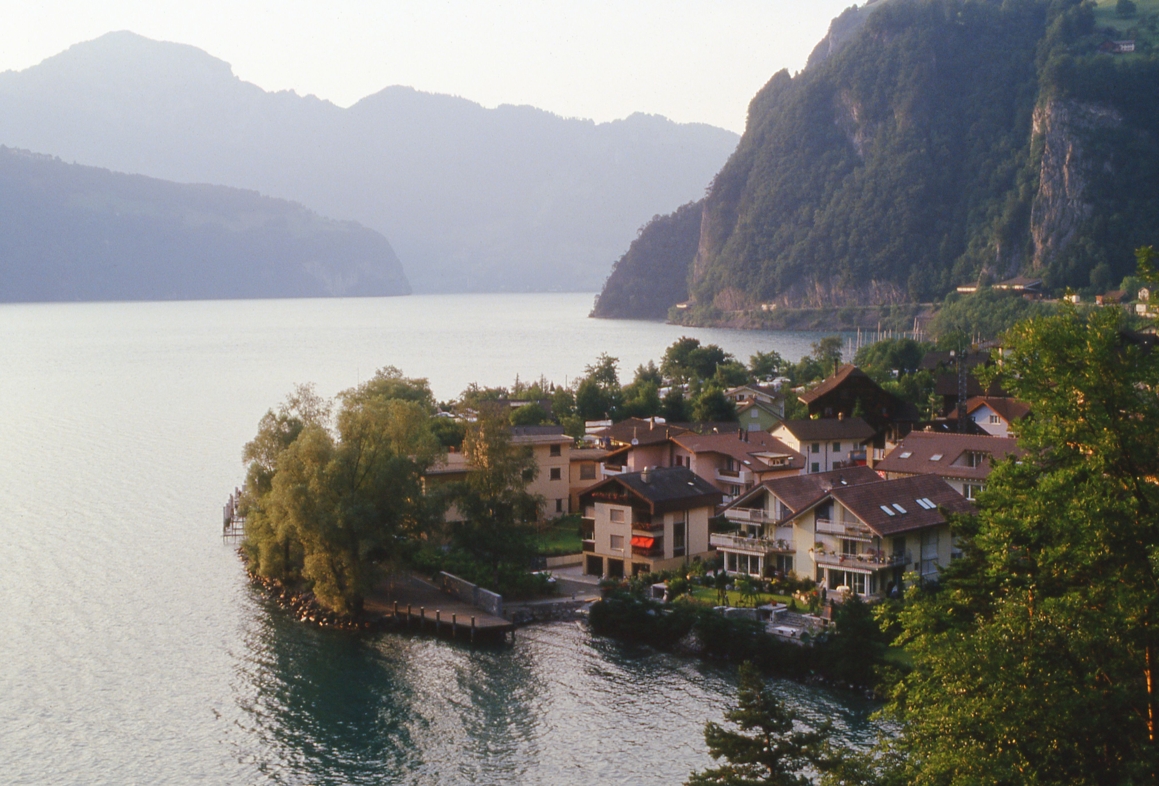 Tranquil Swiss village of Sisikon by Lake Lucerne during twilight with alpine backdrop.