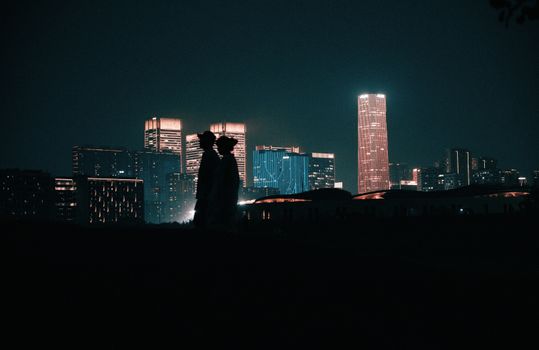A romantic silhouette of a couple against a vibrant city skyline at night.