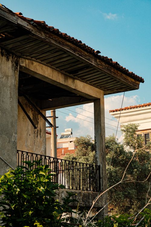 Free An old, abandoned building featuring a weathered balcony and surrounded by greenery under a clear sky. Stock Photo