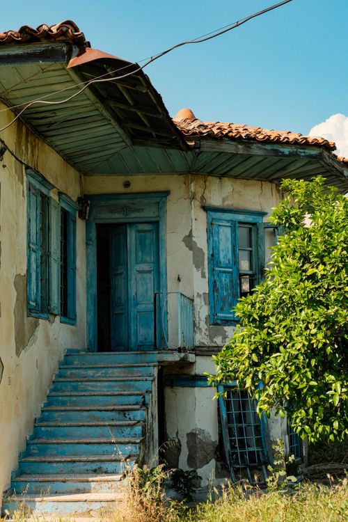 Free Charming old house with blue doors, peeling paint, and overgrown greenery. Stock Photo