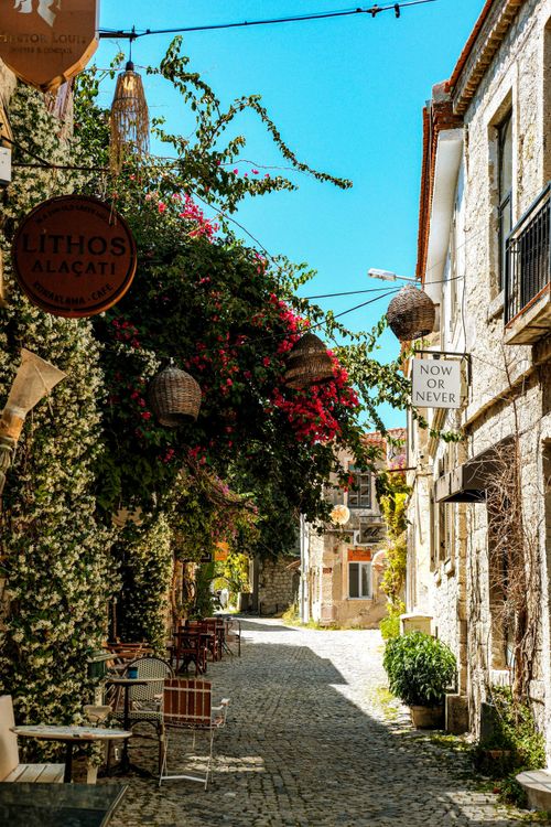 Free A cobblestone street in Alacati, Turkey, lined with colorful bougainvillea. Tranquil and picturesque. Stock Photo