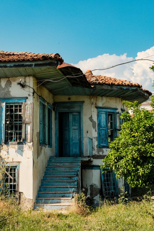 Free Old Mediterranean house with distressed facade and blue shutters, exuding historical charm in a sunny setting. Stock Photo