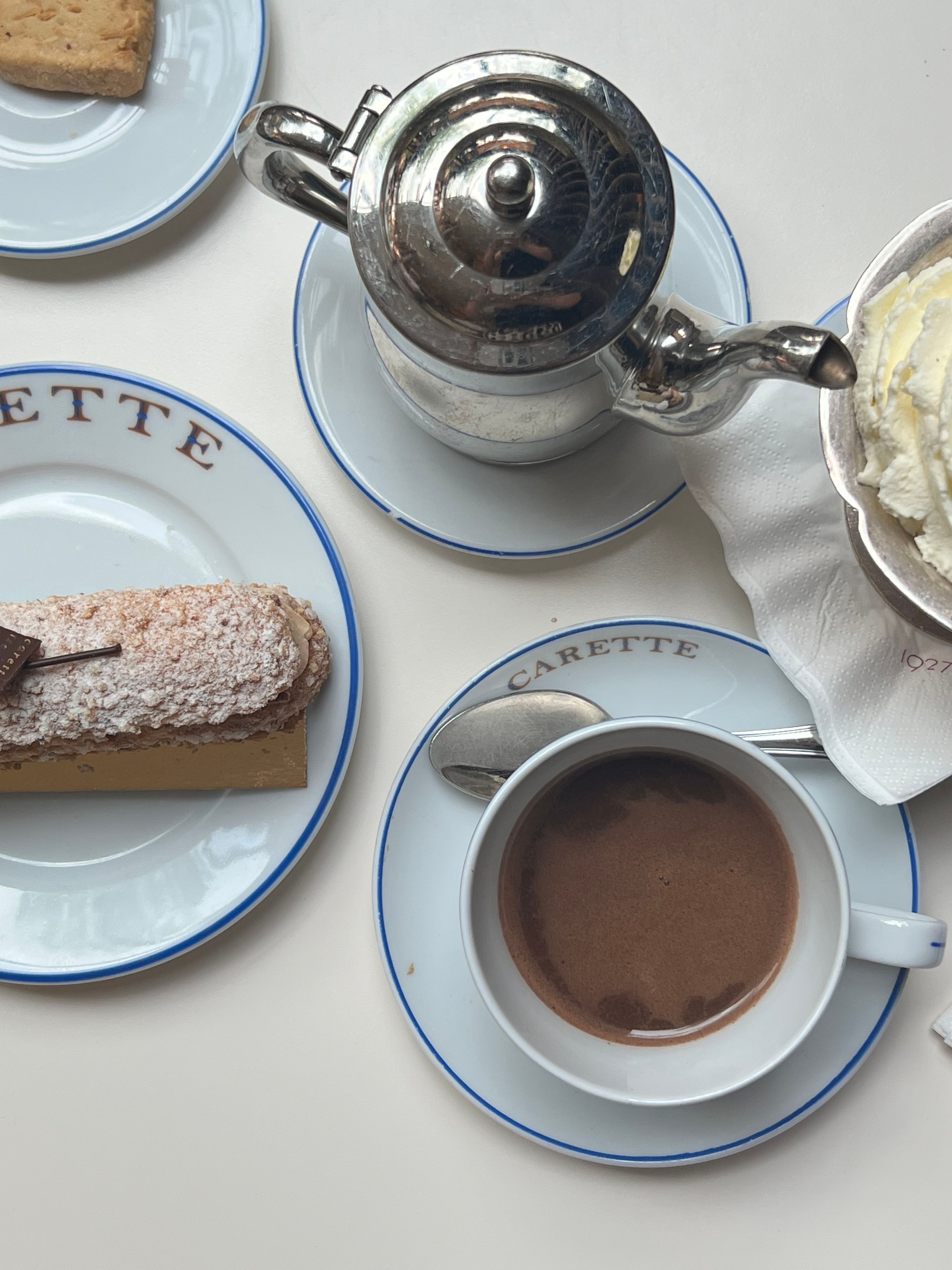 A top-view of a Parisian cafe table set with coffee, whipped cream, and pastries on Carette-branded plates.