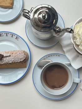 A top-view of a Parisian cafe table set with coffee, whipped cream, and pastries on Carette-branded plates.