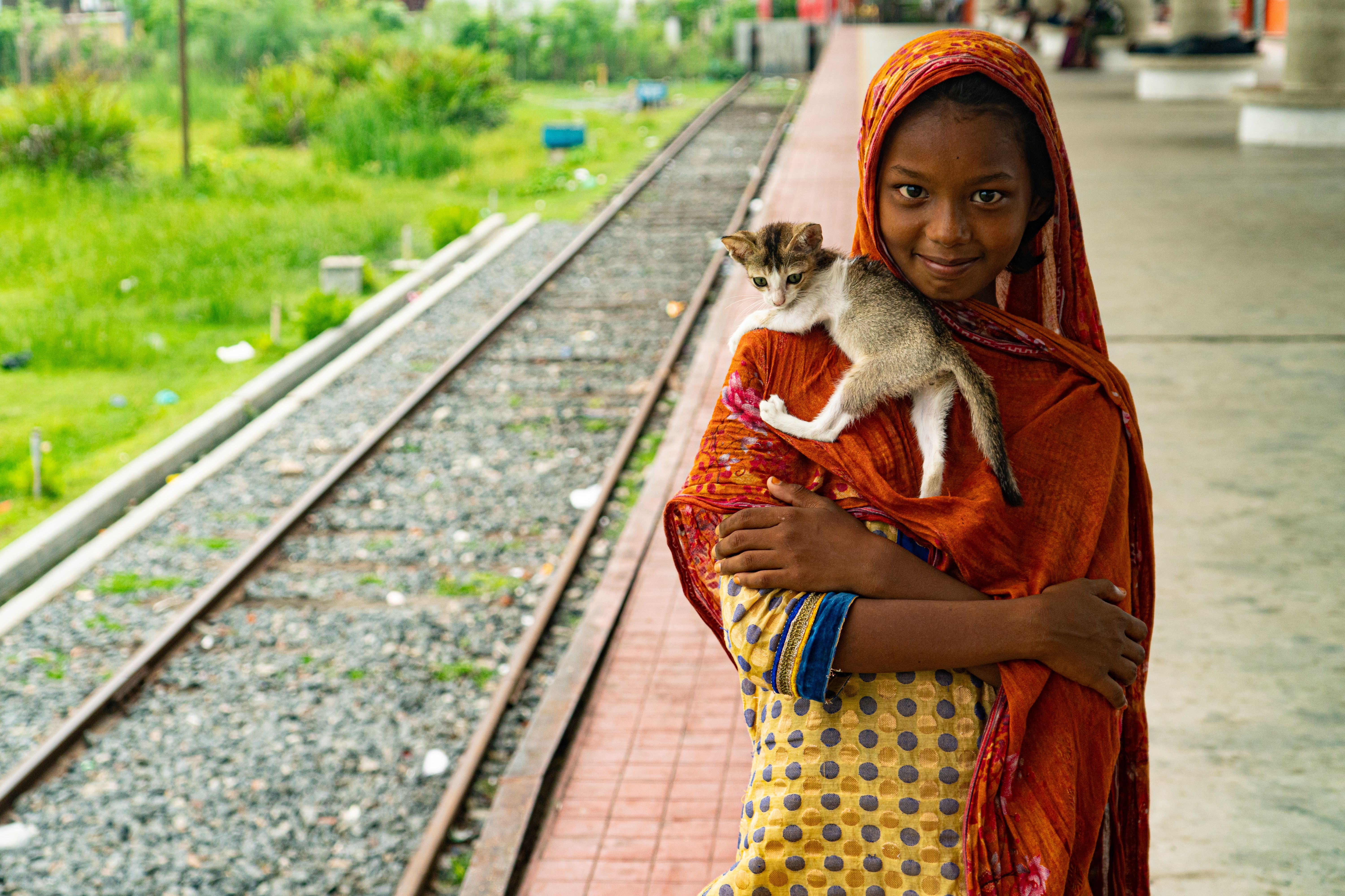 Smiling girl holding a kitten on her shoulder at a train station in Khulna, Bangladesh.