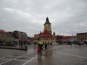 A rainy day captures the charm of Brașov's medieval town square with people holding umbrellas.