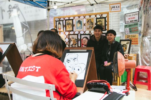 Street artist drawing a caricature for a couple at an outdoor art booth. Vibrant and lively scene.