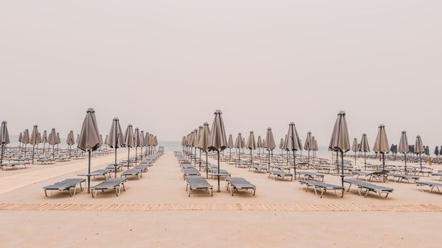 Serene view of empty beach in Rethymno, Greece with aligned sunbeds and umbrellas.